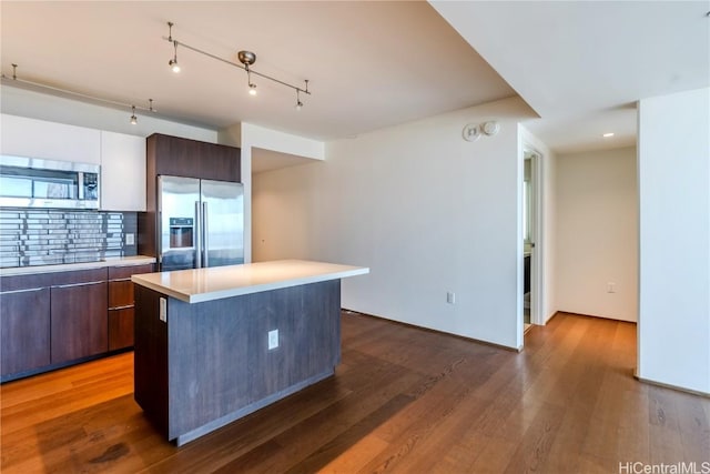 kitchen with appliances with stainless steel finishes, tasteful backsplash, rail lighting, a center island, and dark brown cabinetry