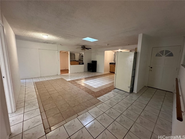 interior space featuring light tile patterned floors, a textured ceiling, a skylight, and ceiling fan