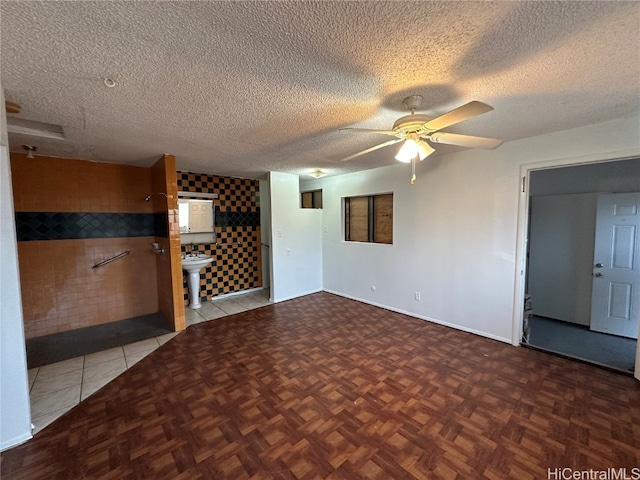 empty room featuring ceiling fan, a textured ceiling, light tile patterned floors, and tile walls