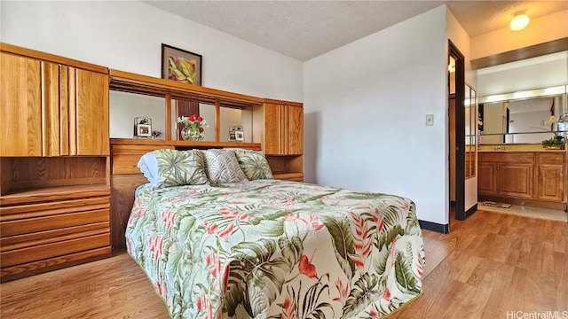 bedroom featuring ensuite bathroom, a textured ceiling, vaulted ceiling, and light hardwood / wood-style flooring