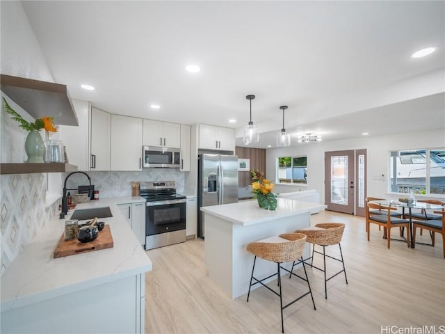 kitchen with sink, a center island, hanging light fixtures, stainless steel appliances, and light wood-type flooring