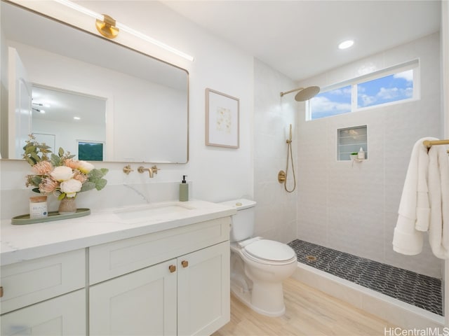 bathroom featuring tiled shower, vanity, hardwood / wood-style flooring, and toilet