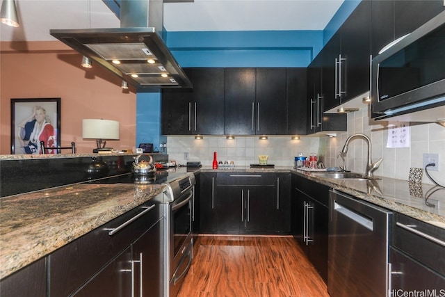 kitchen with appliances with stainless steel finishes, tasteful backsplash, island range hood, dark wood-type flooring, and sink