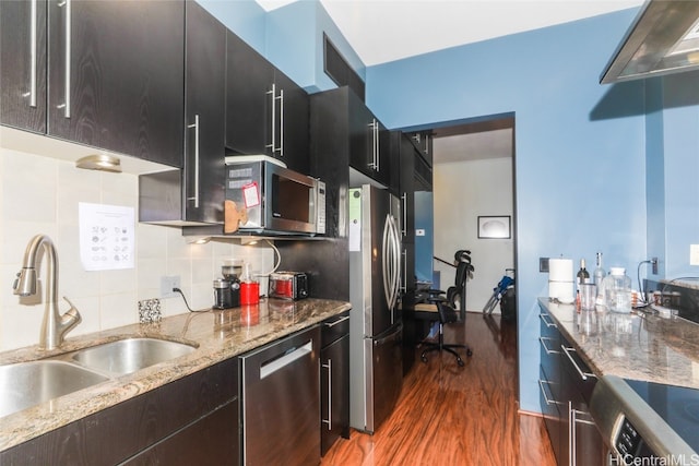 kitchen featuring sink, hardwood / wood-style flooring, light stone countertops, appliances with stainless steel finishes, and tasteful backsplash