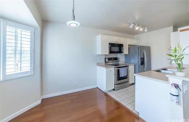 kitchen featuring stainless steel appliances, light wood-type flooring, white cabinetry, decorative light fixtures, and sink