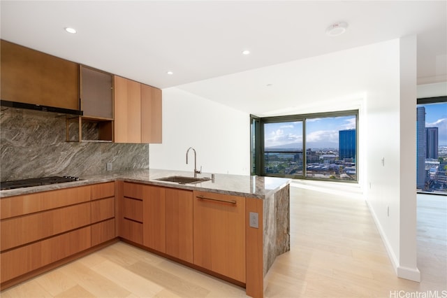 kitchen with stainless steel gas cooktop, kitchen peninsula, sink, and light hardwood / wood-style flooring