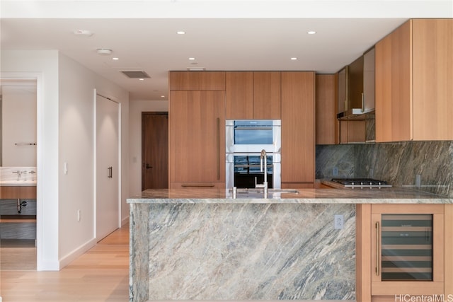 kitchen featuring wall chimney range hood, light hardwood / wood-style flooring, tasteful backsplash, stainless steel appliances, and beverage cooler