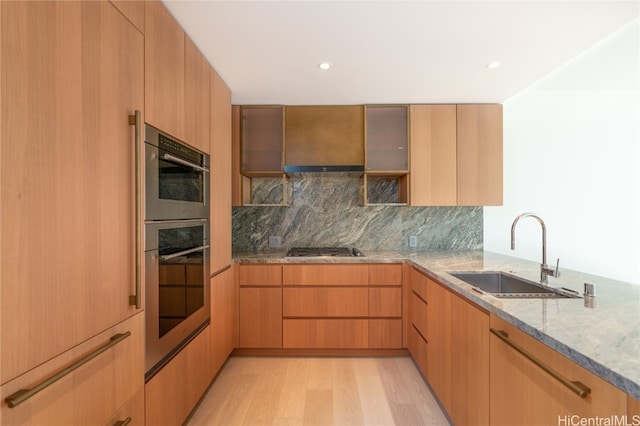 kitchen with light stone countertops, sink, stainless steel appliances, light hardwood / wood-style flooring, and decorative backsplash