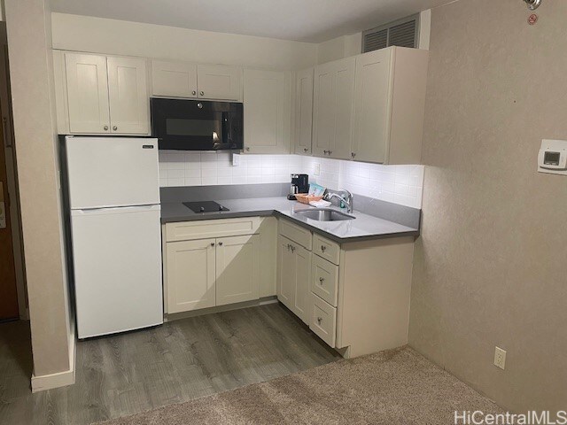 kitchen featuring sink, dark wood-type flooring, decorative backsplash, white cabinets, and black appliances
