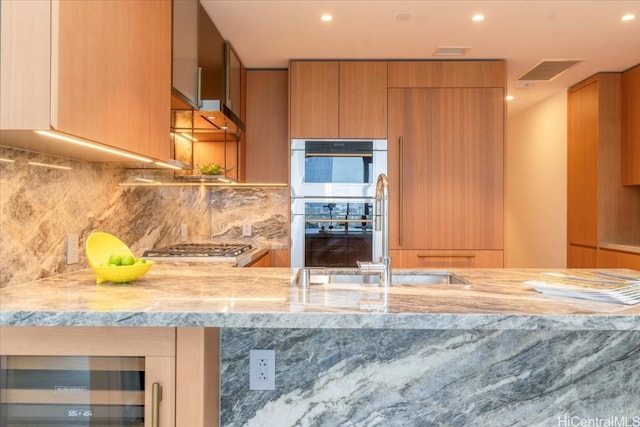 kitchen featuring beverage cooler, light stone counters, appliances with stainless steel finishes, and backsplash