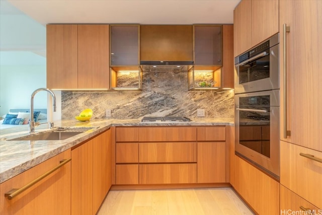 kitchen featuring tasteful backsplash, light wood-type flooring, appliances with stainless steel finishes, light stone countertops, and sink