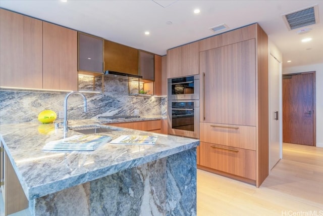 kitchen featuring light wood-type flooring, appliances with stainless steel finishes, light stone countertops, sink, and decorative backsplash