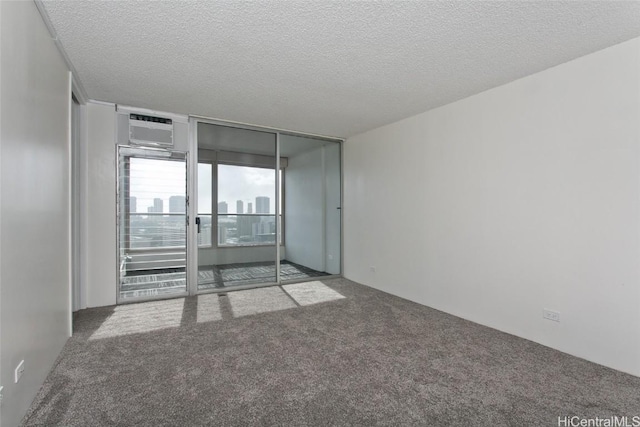 carpeted spare room featuring an AC wall unit, a textured ceiling, and floor to ceiling windows