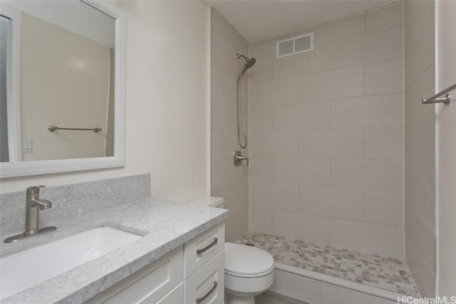 bathroom with a textured ceiling, toilet, vanity, and tiled shower