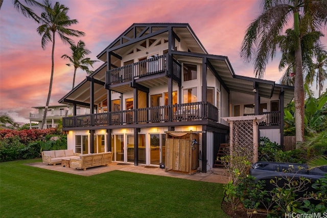 back house at dusk with an outdoor hangout area, a balcony, and a lawn