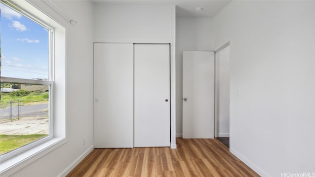 unfurnished bedroom featuring multiple windows, a closet, and light wood-type flooring