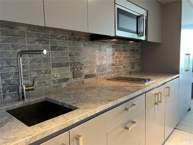 kitchen featuring decorative backsplash, sink, light stone counters, and appliances with stainless steel finishes