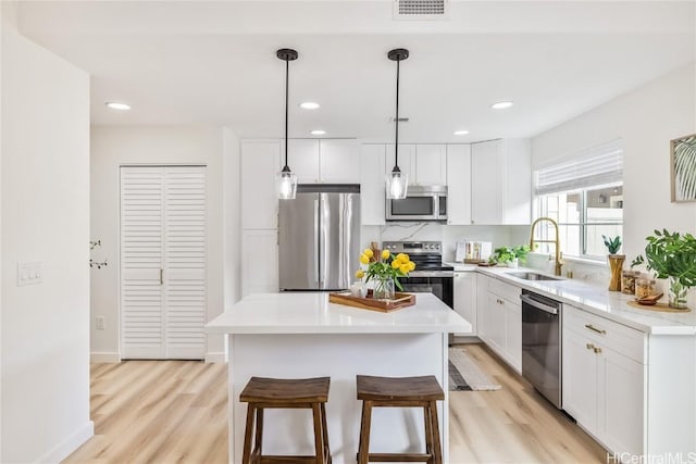 kitchen with appliances with stainless steel finishes, sink, a center island, white cabinetry, and hanging light fixtures