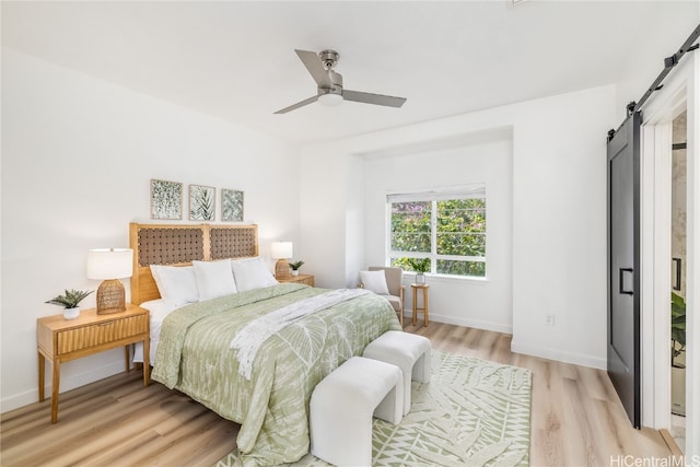 bedroom with a barn door, ceiling fan, and light hardwood / wood-style flooring