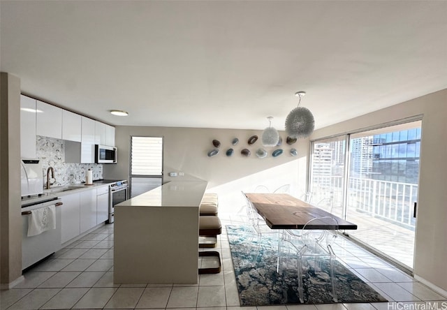 kitchen with stainless steel appliances, tasteful backsplash, light tile patterned floors, white cabinets, and pendant lighting