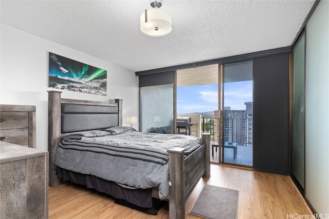 bedroom featuring access to exterior, a textured ceiling, light wood-type flooring, and floor to ceiling windows