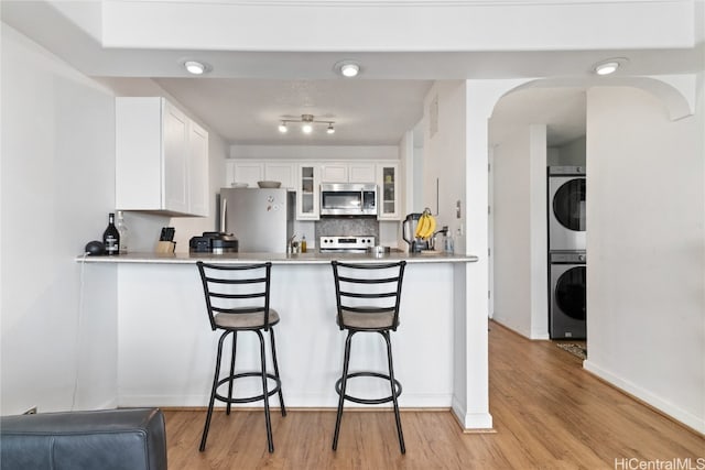 kitchen with light hardwood / wood-style floors, a breakfast bar, appliances with stainless steel finishes, stacked washing maching and dryer, and white cabinets