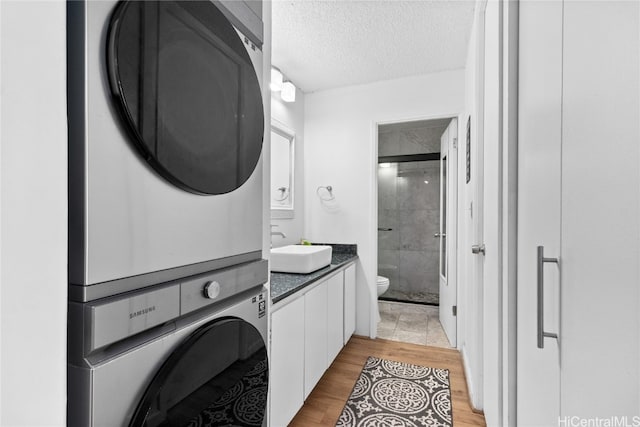 bathroom featuring toilet, a textured ceiling, hardwood / wood-style flooring, stacked washer / dryer, and vanity