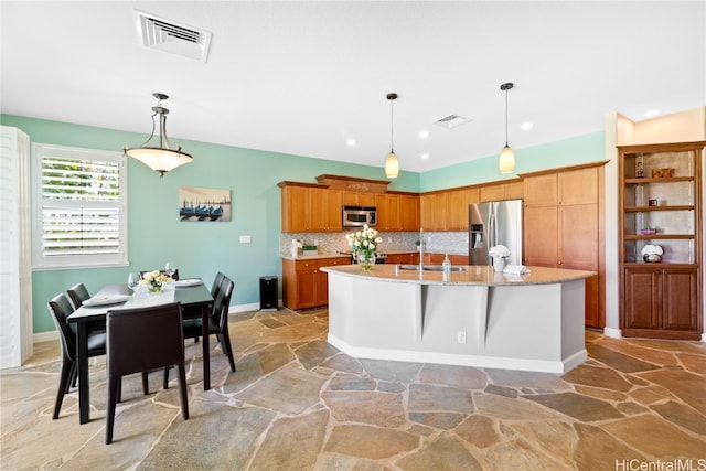 kitchen featuring stainless steel appliances, hanging light fixtures, decorative backsplash, an island with sink, and a kitchen breakfast bar