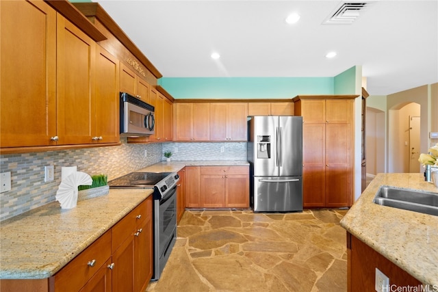 kitchen with appliances with stainless steel finishes, tasteful backsplash, light stone counters, and sink