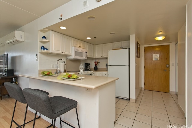 kitchen featuring white cabinetry, a wall mounted air conditioner, kitchen peninsula, white appliances, and a breakfast bar