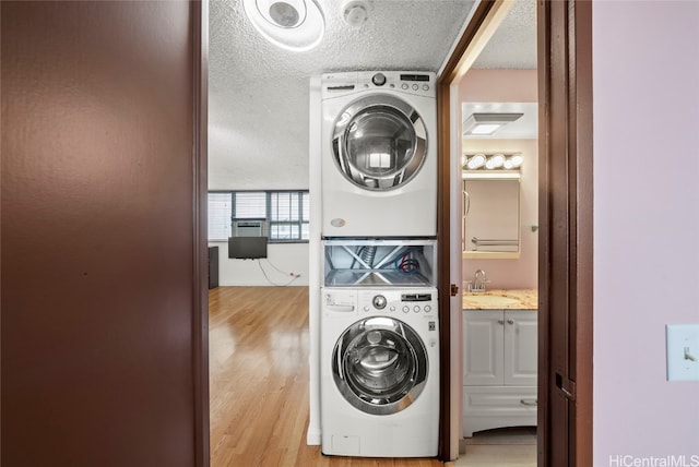 washroom featuring a textured ceiling, sink, light hardwood / wood-style floors, and stacked washer / drying machine