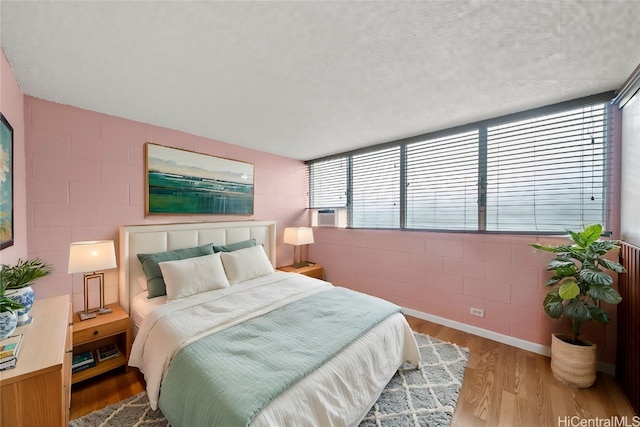 bedroom featuring hardwood / wood-style floors, a textured ceiling, multiple windows, and cooling unit