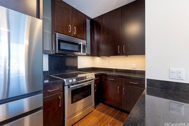 kitchen with dark stone countertops, dark wood-type flooring, dark brown cabinets, and stainless steel appliances