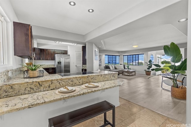 kitchen featuring dark brown cabinetry, light stone counters, kitchen peninsula, stainless steel refrigerator with ice dispenser, and light hardwood / wood-style flooring