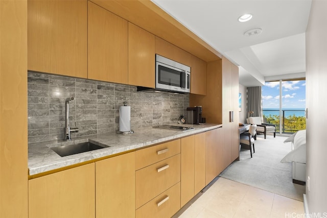 kitchen featuring light stone counters, backsplash, sink, a water view, and light colored carpet