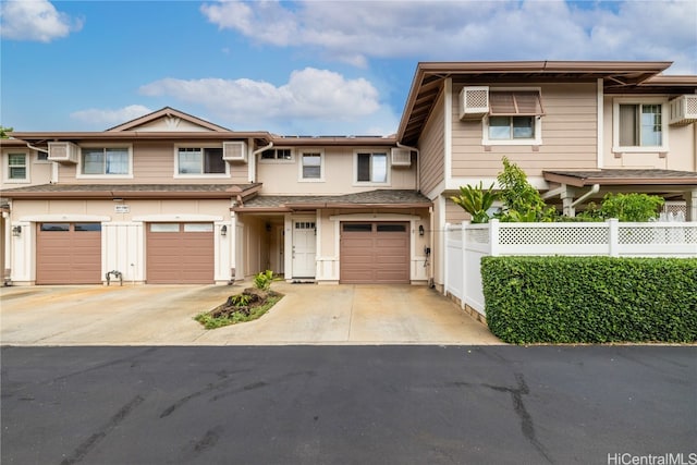 view of property with a garage, an AC wall unit, driveway, and fence