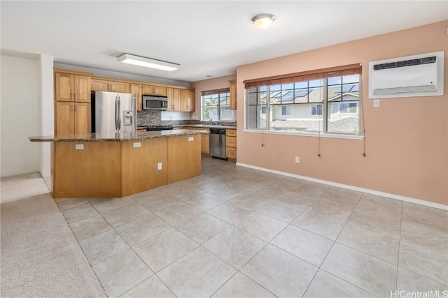 kitchen with dark stone countertops, appliances with stainless steel finishes, brown cabinetry, and an AC wall unit