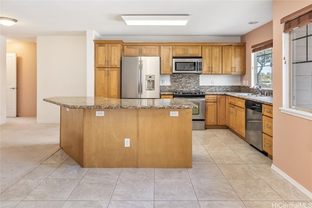 kitchen featuring light tile patterned floors, stainless steel appliances, stone countertops, a kitchen island, and a sink