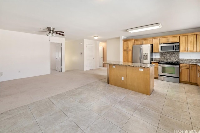 kitchen with light stone counters, stainless steel appliances, light colored carpet, backsplash, and a kitchen island