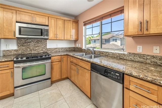 kitchen featuring light tile patterned floors, dark stone counters, appliances with stainless steel finishes, brown cabinets, and a sink