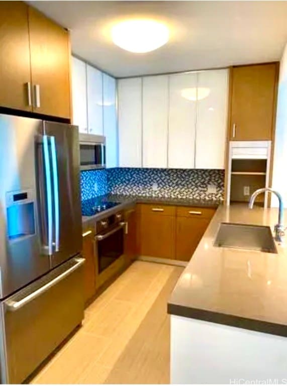 kitchen featuring stainless steel appliances, kitchen peninsula, sink, tasteful backsplash, and light wood-type flooring