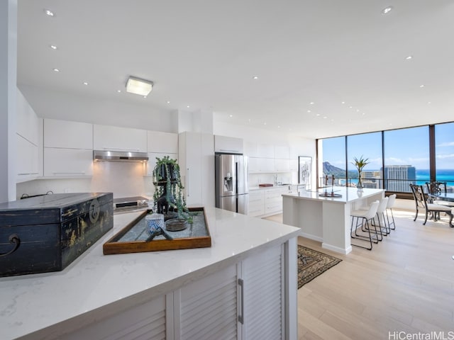 kitchen with a breakfast bar, stainless steel fridge, light hardwood / wood-style flooring, and white cabinetry