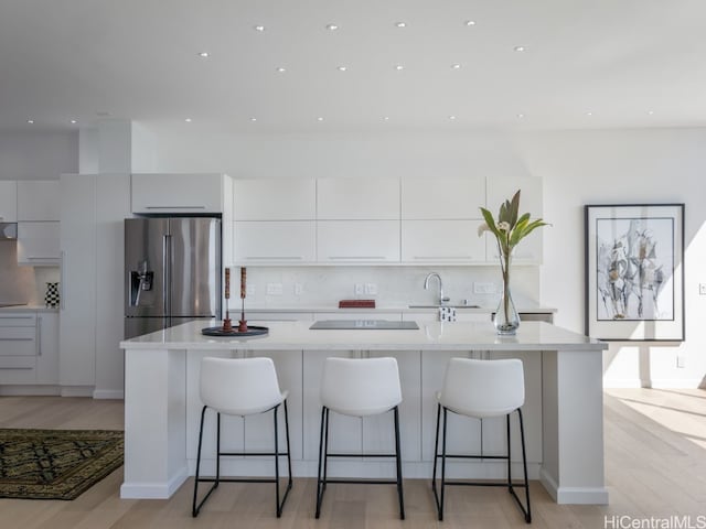 kitchen with white cabinetry, stainless steel refrigerator with ice dispenser, a breakfast bar area, and light hardwood / wood-style flooring