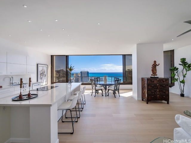 kitchen with a kitchen breakfast bar, a water view, black electric cooktop, light hardwood / wood-style floors, and white cabinetry