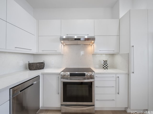 kitchen with light wood-type flooring, appliances with stainless steel finishes, light stone counters, white cabinetry, and extractor fan