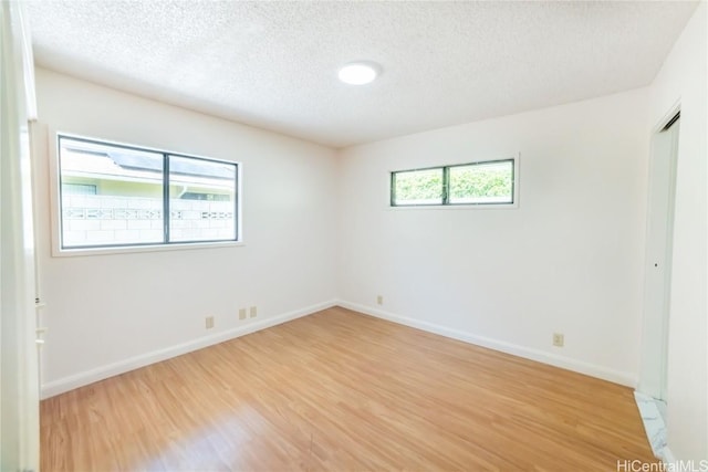 empty room with a healthy amount of sunlight, light hardwood / wood-style floors, and a textured ceiling