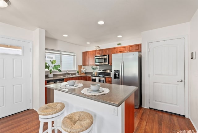 kitchen with a kitchen bar, appliances with stainless steel finishes, dark wood-type flooring, sink, and a center island