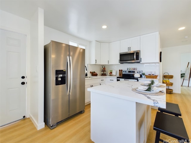 kitchen with light hardwood / wood-style flooring, appliances with stainless steel finishes, light stone counters, and white cabinets