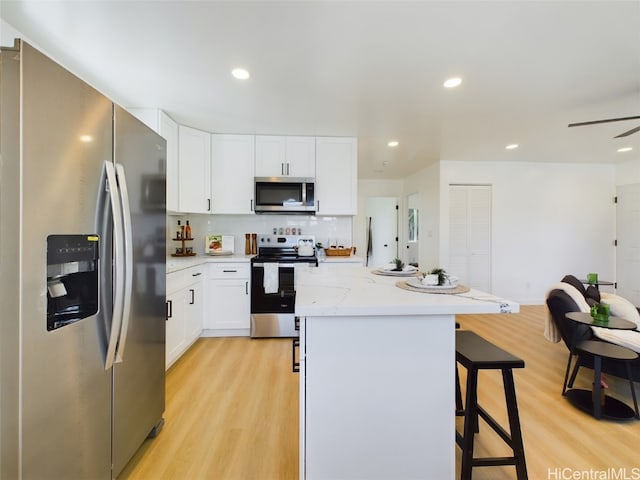 kitchen featuring stainless steel appliances, light hardwood / wood-style floors, white cabinetry, a breakfast bar, and a kitchen island