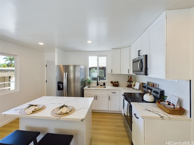 kitchen with light hardwood / wood-style floors, sink, appliances with stainless steel finishes, a kitchen bar, and white cabinets